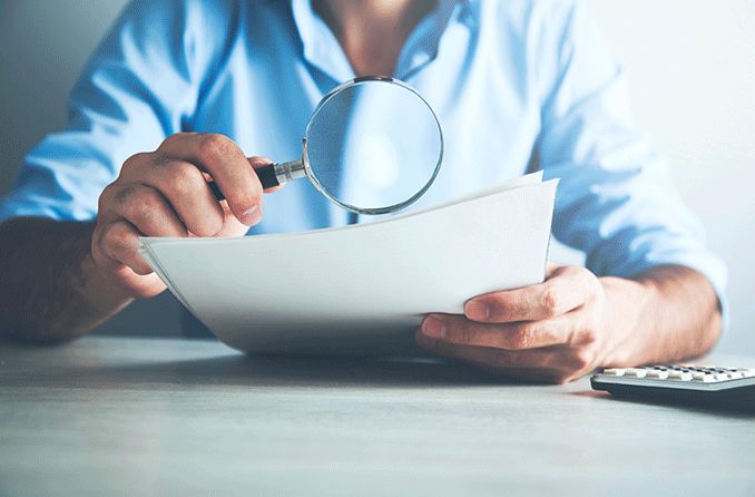 man looking at papers through a magnifying glass