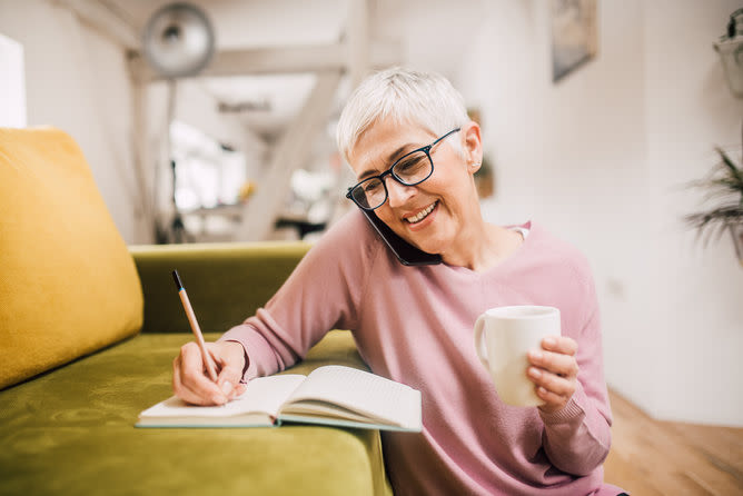 personne souriante au téléphone pendant qu'elle écrit quelque chose