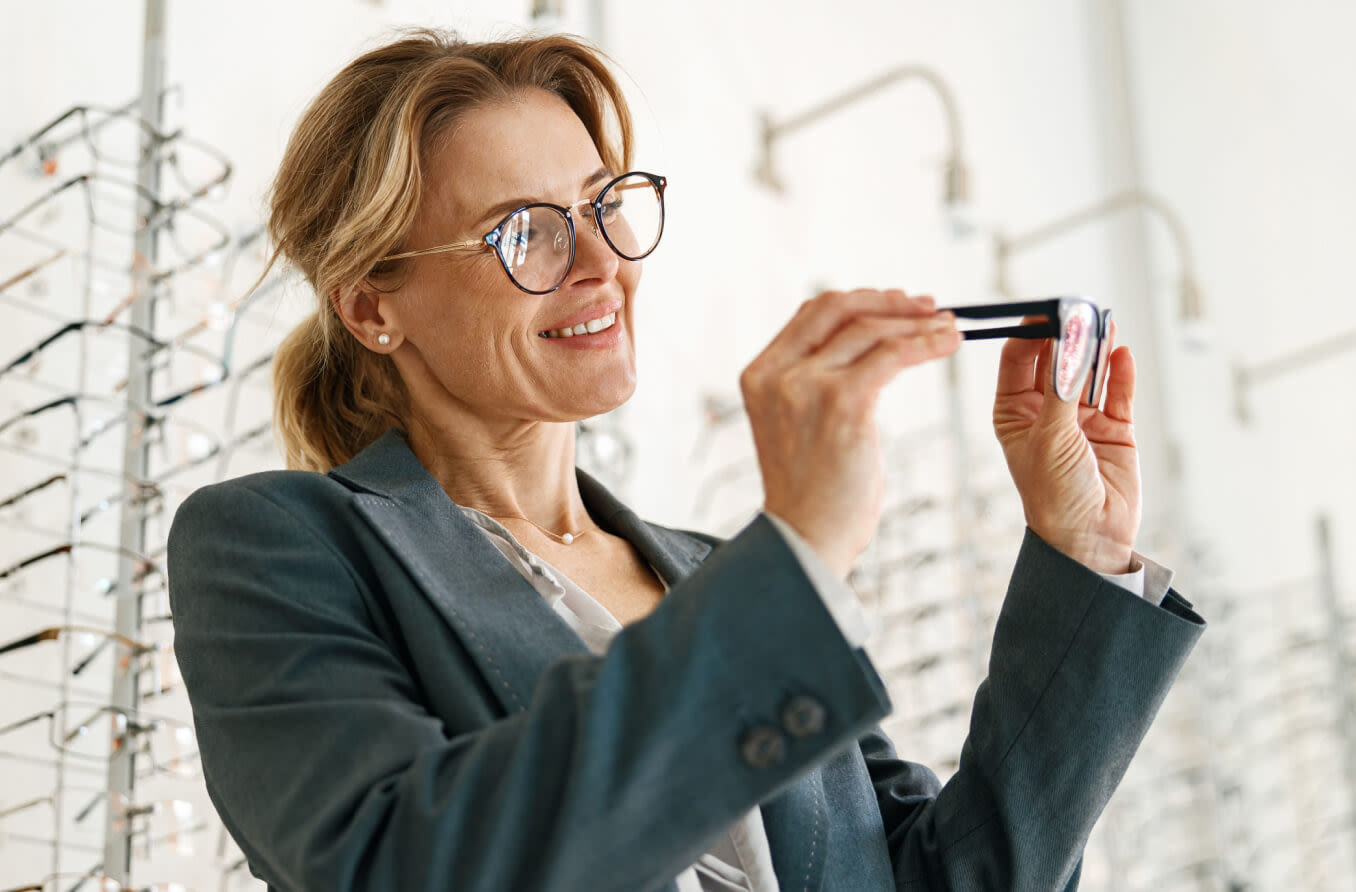Woman chooses between two glasses in an optician's shop.