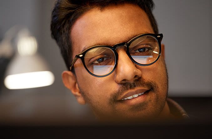 man wearing eyeglasses with computer screen in reflection of eyeglass lenses