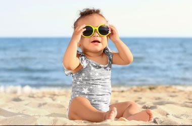 Baby on the beach, wearing sunglasses.