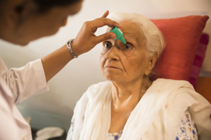 An older Indian woman getting eye drops put in her eye by an eye doctor.