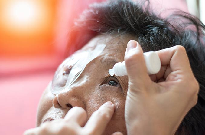 Một y tá bôi thuốc nhỏ mắt chữa bệnh đục thủy tinh thể vào mắt cho một bệnh nhân lớn tuổi.