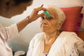 Un'infermiera Che Applica gocce oculari per la cataratta agli occhi occhi di un paziente anziano。