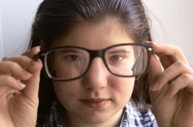 Mädchen hält Brille hoch und schaut durch die Gläser