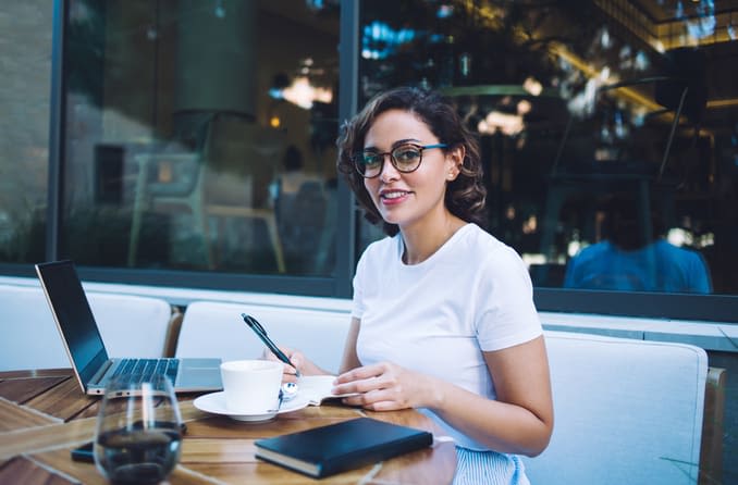 Junge Frau mit Brille arbeitet im Freien an einem Laptop