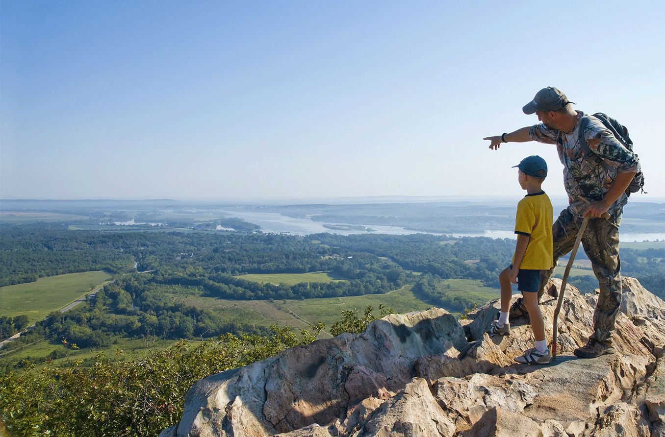 father pointing to horizon with son on top of a mountain