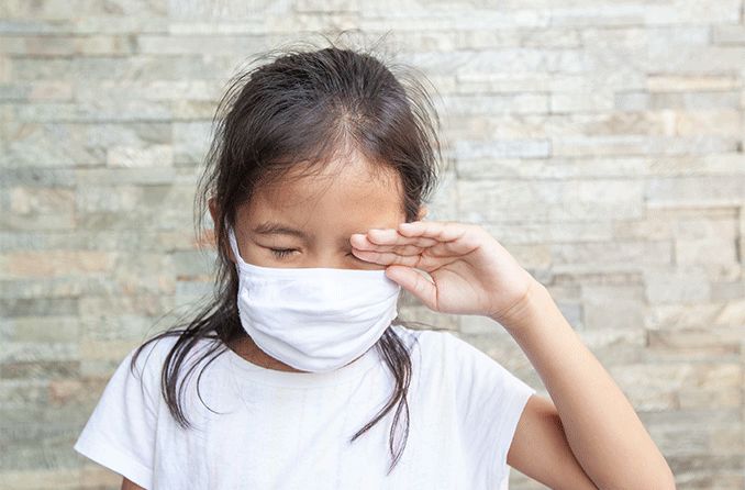 young girl wearing a face mask with sore eyes due to covid