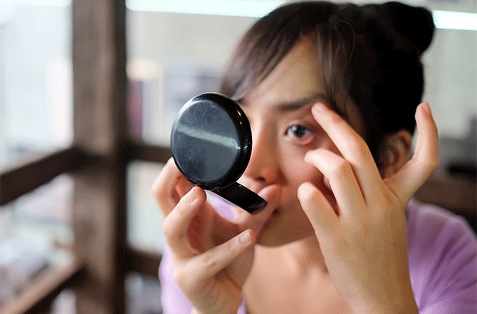 woman looking at a compact mirror trying to get something out of her eye