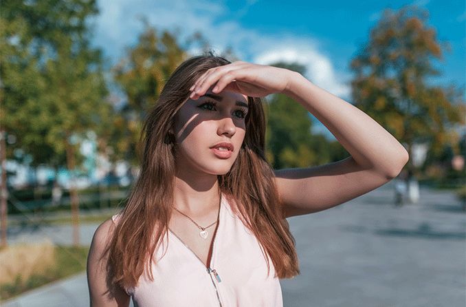 woman looking up at sun shielding her eyes with her hand