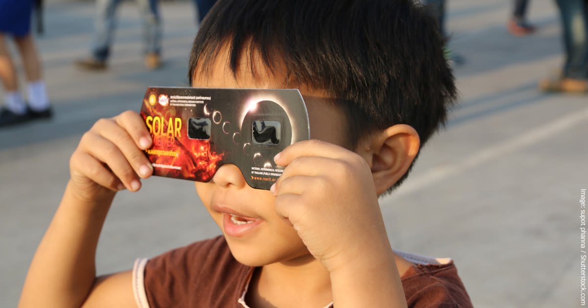  Niño pequeño que mira a través de los vidrios del eclipse que miran para arriba un eclipse solar.