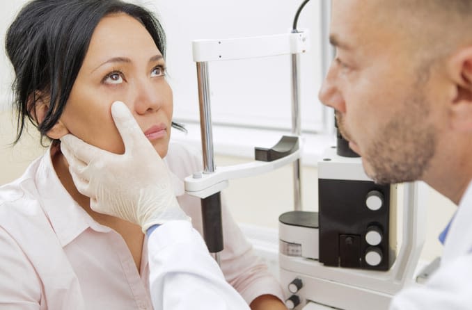 A dark-haired woman calmly looks toward the ceiling so her optometrist can examine her eyes. 