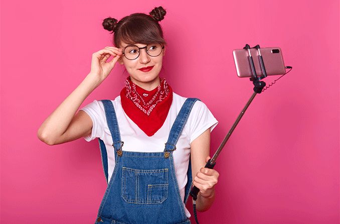 teen girl taking a selfie with her new eyeglasses on a pink background