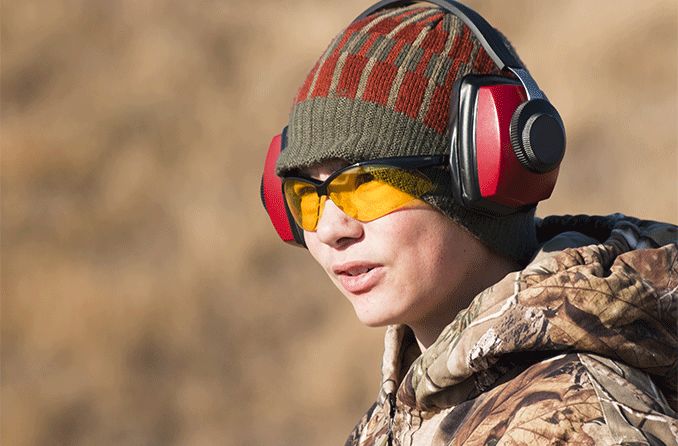 boy wearing noise-canceling headset and prescription shooting glasses