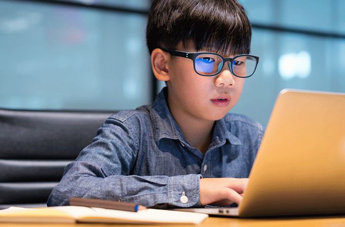young boy wearing blue light blocking glasses looking at laptop screen