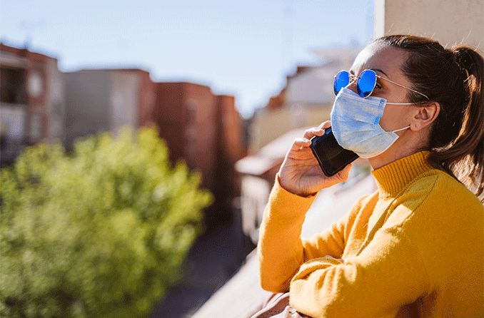 woman during pandemic outside on balcony wearing face mask and sunglasses