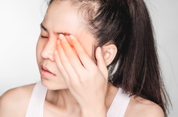 A young woman experiencing eye discomfort gently covers her eye with her hand