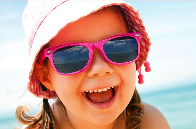 Enfant portant des lunettes de soleil et un chapeau de soleil à la plage.
