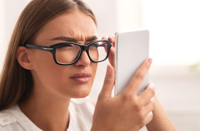 Mujer entrecerrando los ojos a través de sus anteojos mirando teléfonos inteligentes.