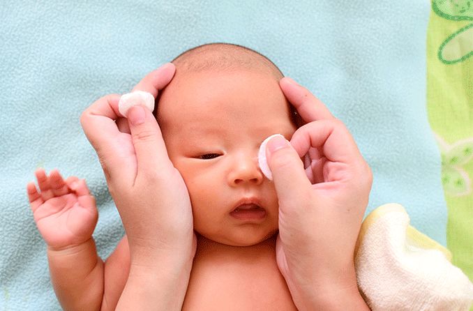 mère essuyant les écoulements oculaires de bébé avec un coton