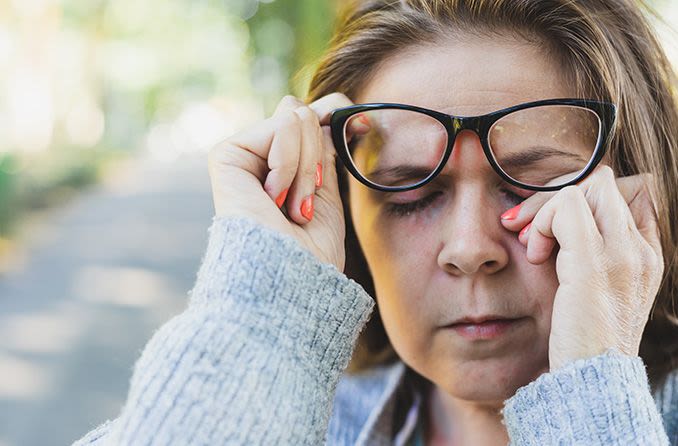 woman wearing eyeglasses rubbing her eye