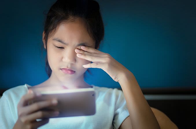 young girl with irritated eyes looking at her mobile phone
