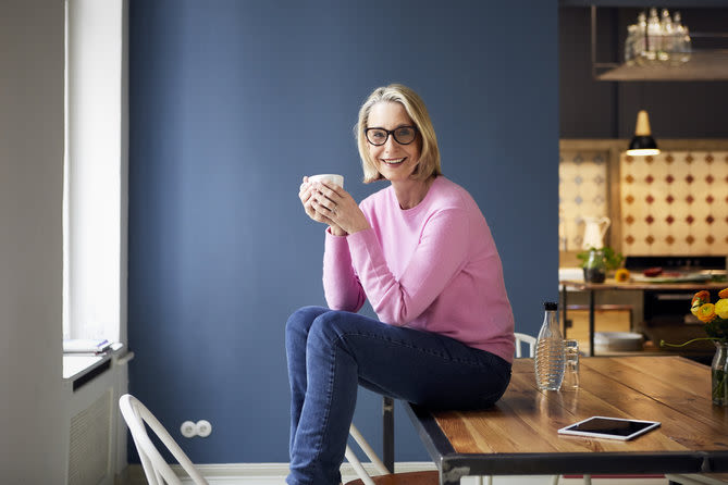 personne souriante avec des lunettes assise sur une table et buvant une boisson