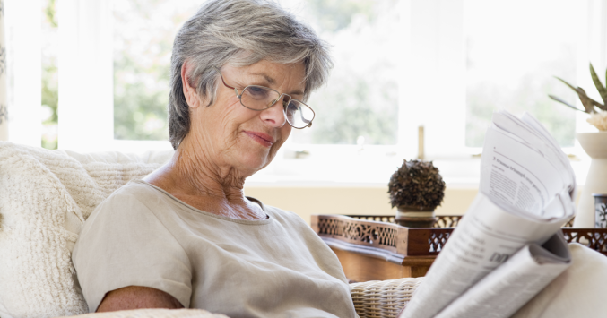 senior woman wearing glasses reading the newspaper