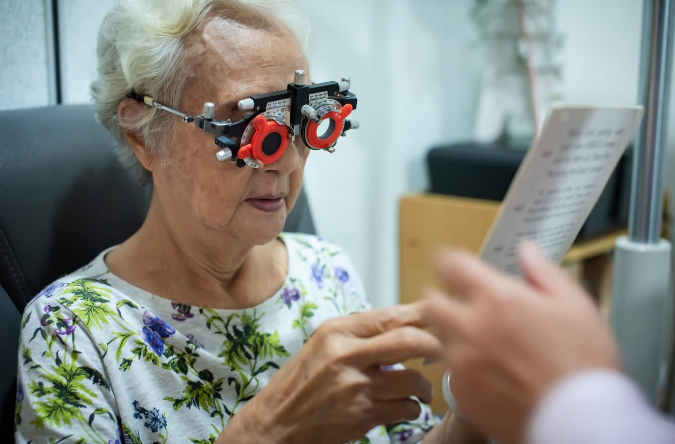 Optometrist using phoropter to check eyesight value for a senior woman