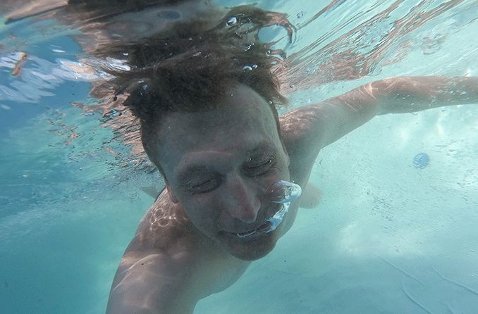 man in ocean with eyes closed due to salt water burning his eyes