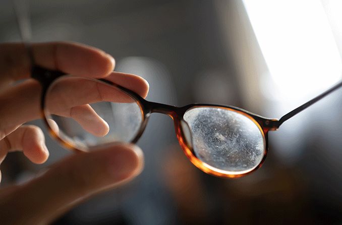 hand holding up a pair of scratched eyeglass lenses