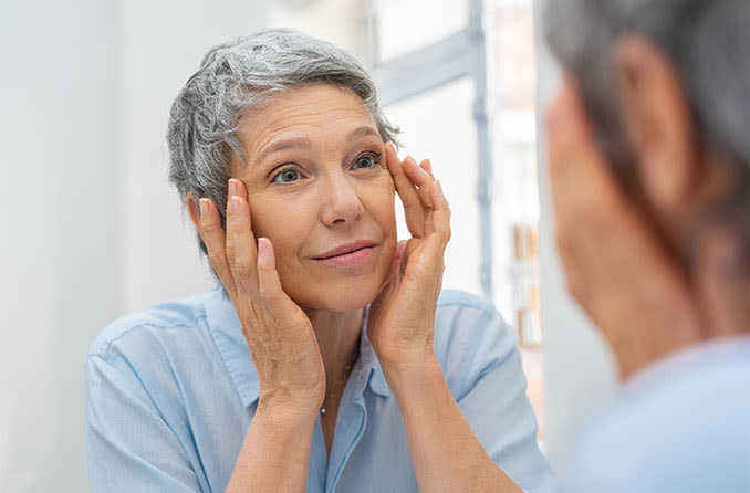 woman looking in the mirror wondering what caused her drooping eyelids (ptosis)