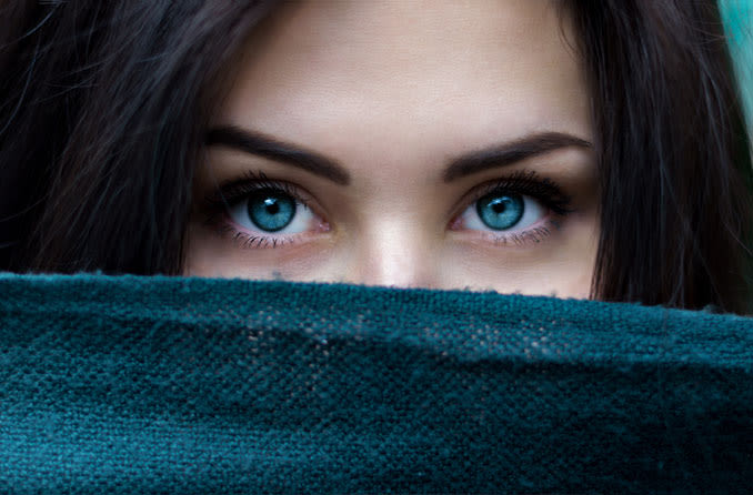 Mulher com olhos azuis cobrindo rosto até o nariz com lenço

