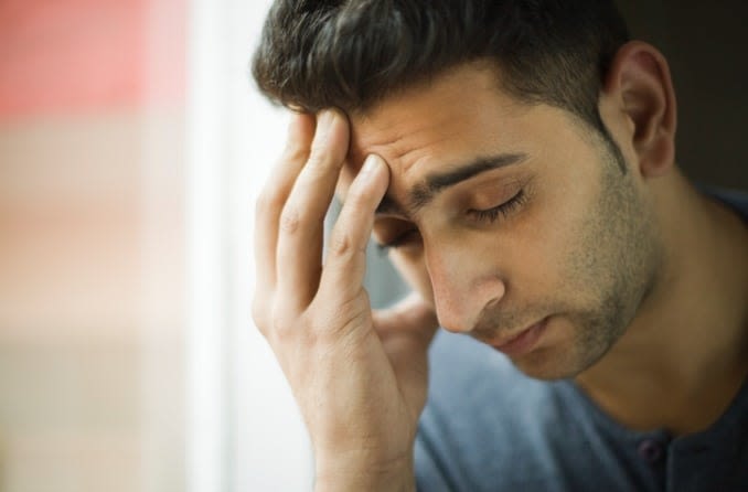 Headache causes a dark-haired young man to close his eyes and massage his forehead.