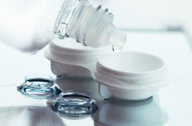 Contact lens solution being poured into a contact lens case with a pair of contacts in the foreground.