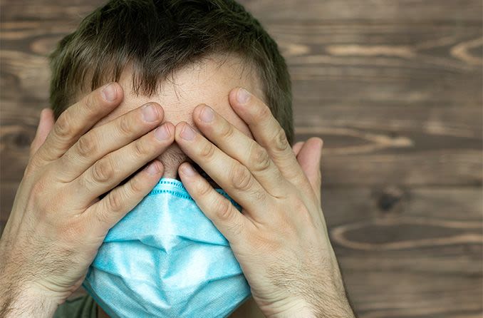 a man wearing a surgical mask with coronavirus touching his eyes