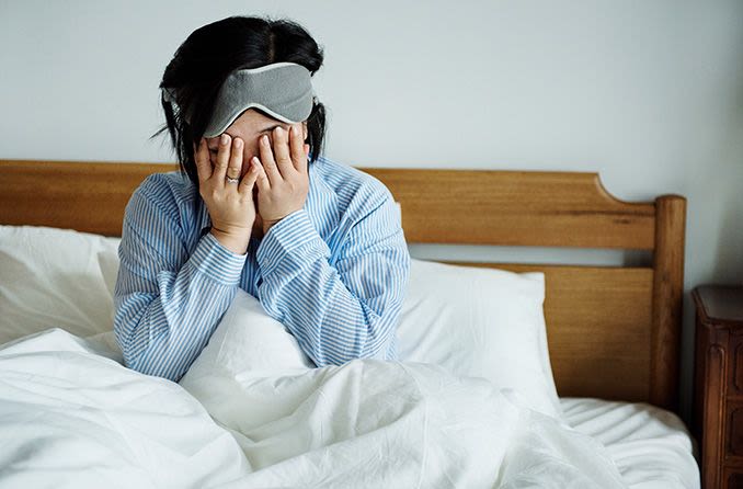 woman in bed rubbing eyes wearing sleep mask