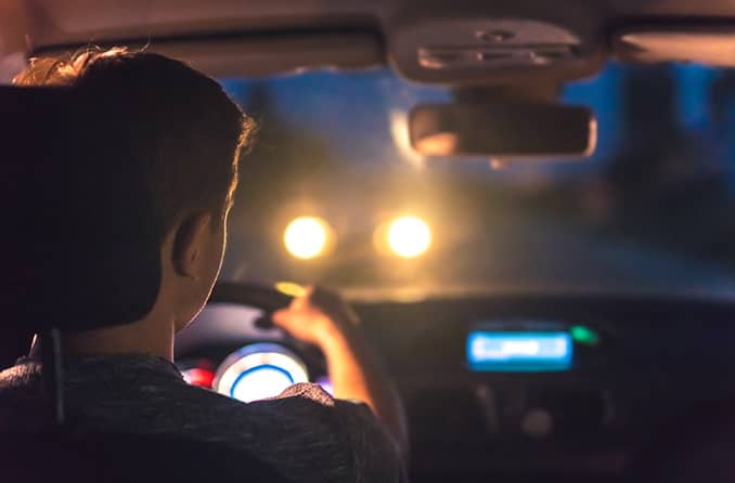 hombre conduciendo de noche con astigmatismo mirando los faros deslumbrantes de un automóvil que conduce hacia él