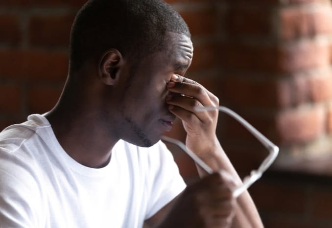 Young man with asthenopia (eye strain) holds his glasses and rubs his eyes.