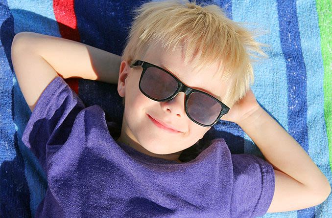 boy laying on beach towel wearing sunglasses