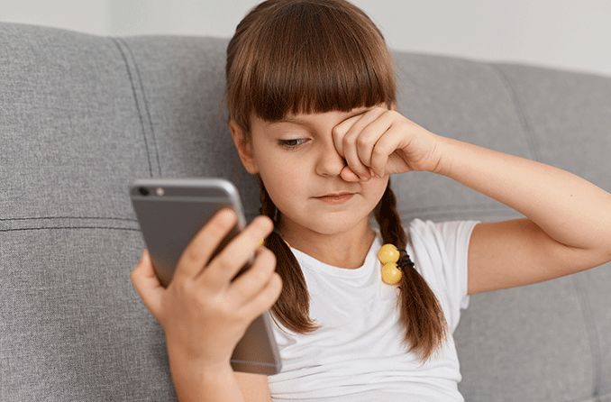 girl on mobile phone rubbing her eyes from too much screen time