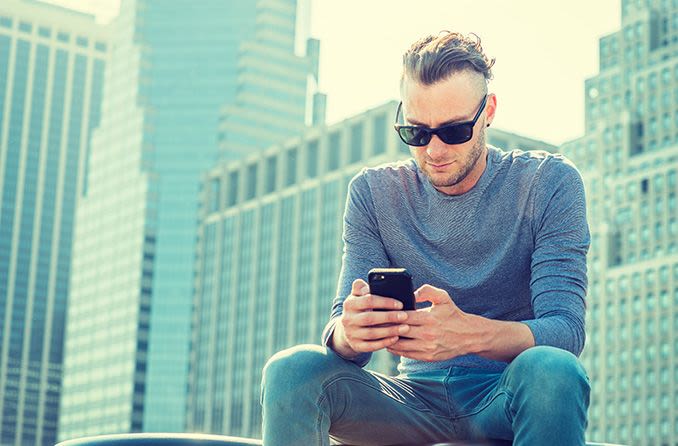 Homme portant des lunettes de soleil progressives à l'extérieur en regardant un téléphone portable