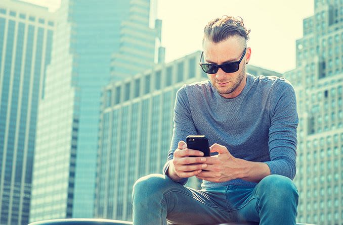 Mann mit progressiver Sonnenbrille im Freien, der auf sein Mobiltelefon schaut