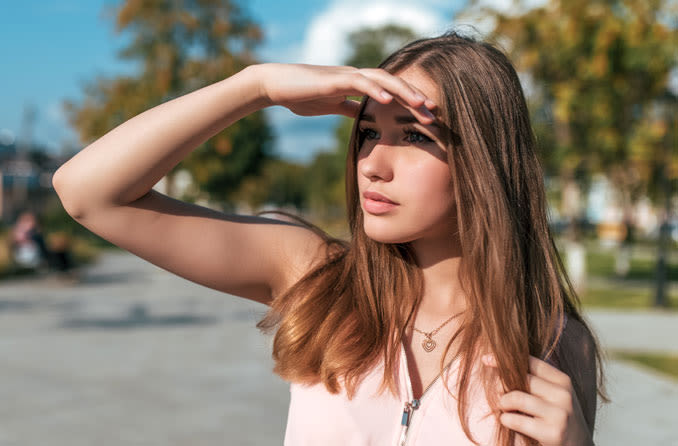 Garota asiática tapando o sol do rosto com as mãos por causa da fotofobia
