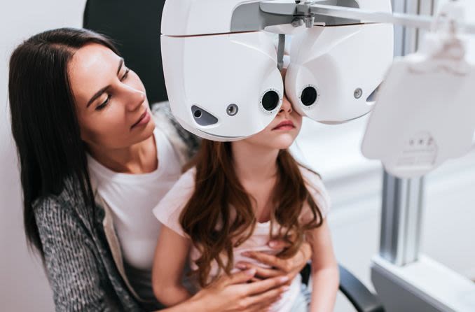 فتاة صغيرة تجلس في حضن والدتها لإجراء فحص للعين