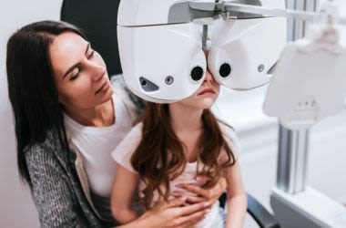 junges Mädchen sitzt auf Mamas Schoß und bekommt eine Augenuntersuchung