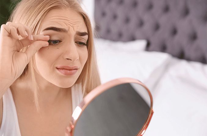 worried woman pulling out her eyelashes looking in a mirror