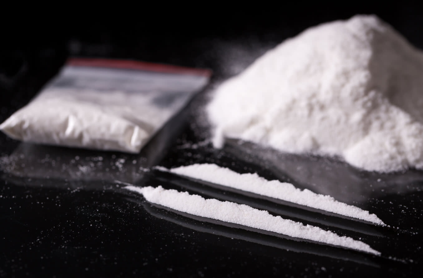 Plastic packet, two lines and pile of cocaine on black background, closeup.