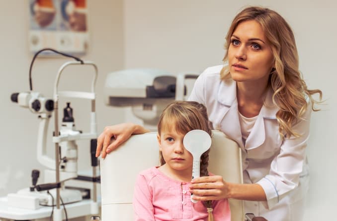 An ophthalmic technician performs a routine eye exam on a little girl.