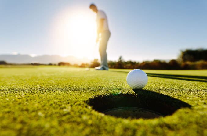 A man wearing sunglasses plays golf.